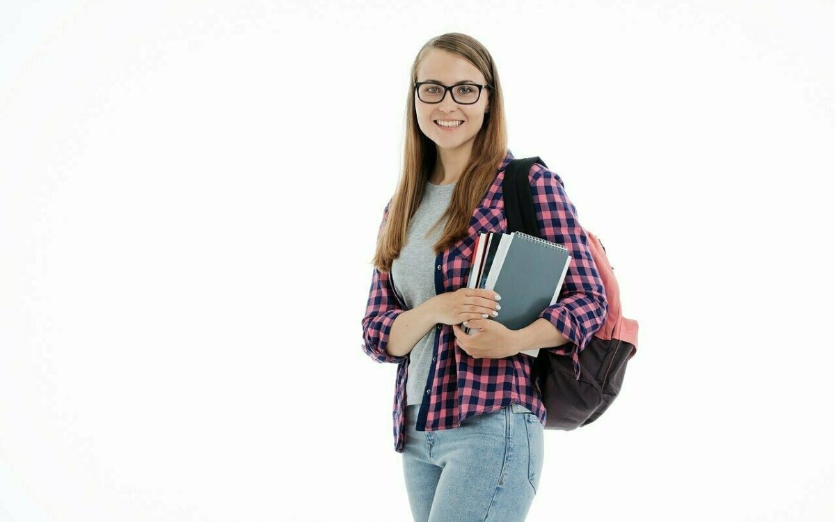 Eine junge Frau mit Rucksack auf dem Rücken und Büchern im Arm lächelt in die Kamera Eine junge Frau mit Rucksack auf dem Rücken und Büchern im Arm lächelt in die Kamera